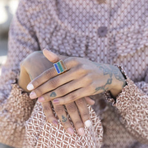 manos de mujer con tres anillos dorados juntos con detalles azul, verde y marron