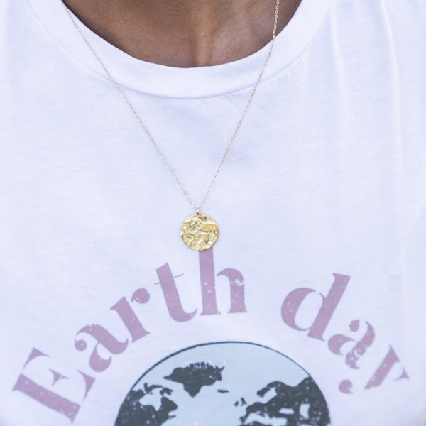 torso de mujer con camiseta blanca y collar dorado con colgante en forma de planeta tierra
